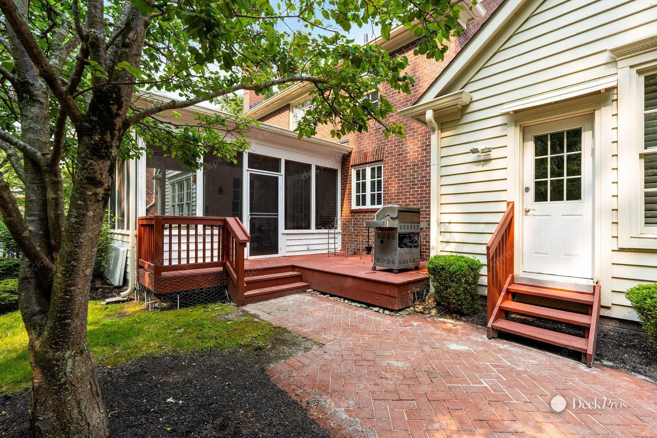 The Anderson deck before work: a low deck and two sets of steps stained rust-red, with matching red railings, beside a faded brick paver patio and a screened porch.
